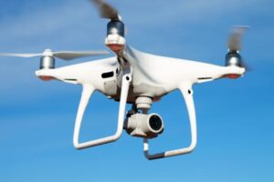 pexels photo 4355183 4355183 A white drone flying against a clear blue sky, capturing aerial views with its camera.